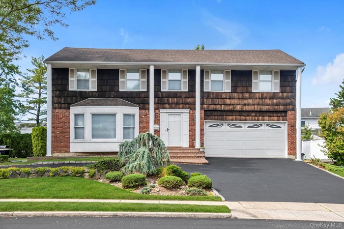 View of front facade with asphalt driveway, a shingled roof, an attached garage, and a front lawn