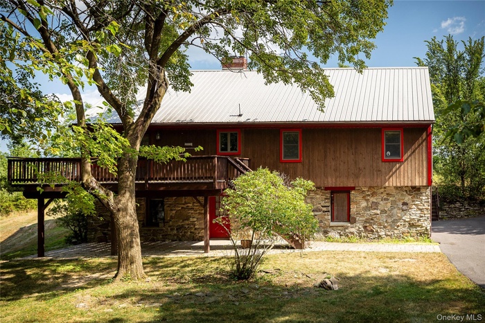 Back of property featuring stone siding, a patio, a metal roof, a wooden deck, and a yard