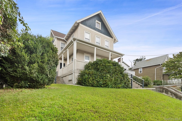 View of front of home with covered porch, a front yard, stairway, and stucco siding