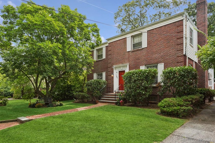 Colonial-style house with brick siding, a chimney, and a front yard
