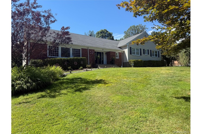 Split level home featuring roof with shingles, a front yard, brick siding, and covered porch