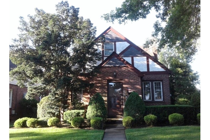 Stately English Tudor/Cape style home featuring a front lawn
