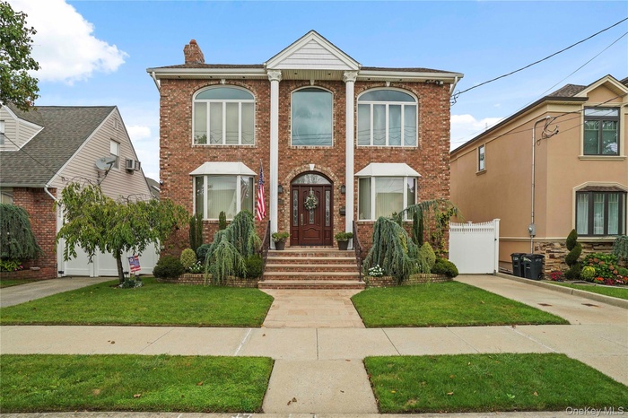 Greek revival house featuring a chimney, brick siding, and a front yard