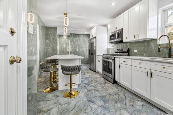 Kitchen featuring appliances with stainless steel finishes, light marble finish flooring, a sink, white cabinetry, and light countertops