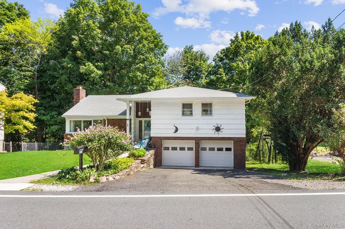 Split level home featuring brick siding, asphalt driveway, a front lawn, an attached garage, and view of scattered trees