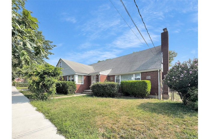 View of front facade with a chimney, a front yard, brick siding, and a shingled roof