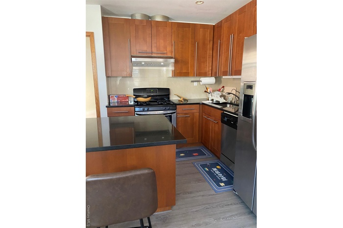 Kitchen with stainless steel range oven, a kitchen breakfast bar, light wood-style flooring, decorative backsplash, and brown cabinets