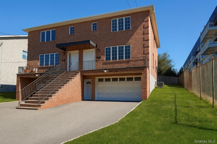 View of front facade featuring stairs, brick siding, asphalt driveway, a front lawn, and a garage