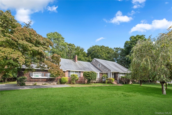 Cape Cod-style house featuring a front yard, a chimney, and view of wooded area