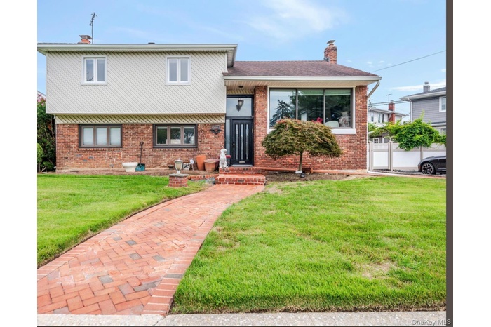 Tri-level home with a chimney, brick siding, a front yard, and roof with shingles