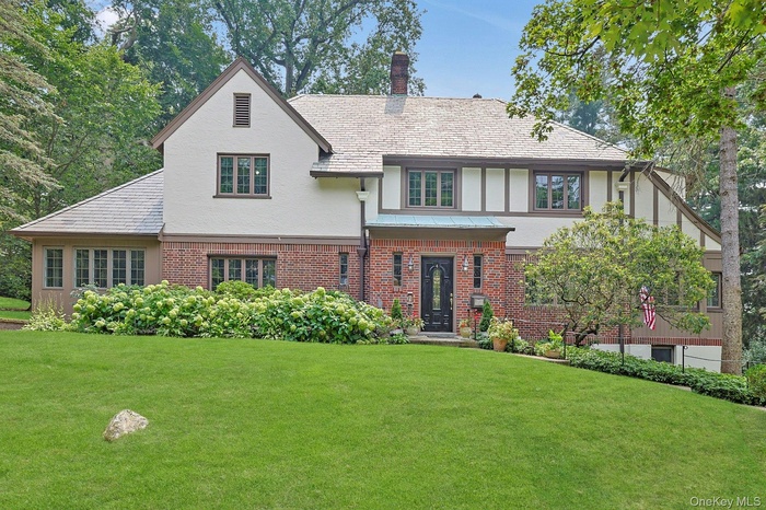 Tudor-style house featuring a front lawn, stucco siding, brick siding, and a chimney