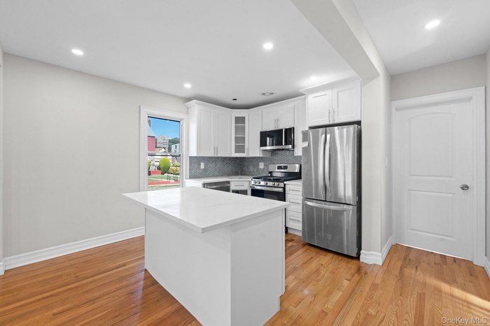 Kitchen featuring stainless steel appliances, backsplash, white cabinetry, glass insert cabinets, and a kitchen island