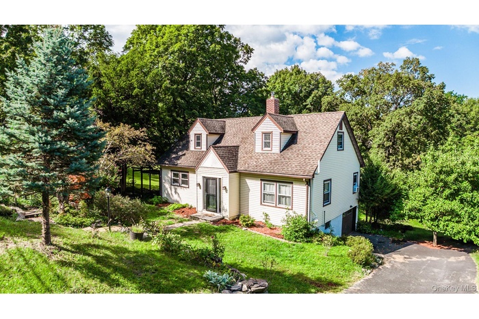Cape cod house with driveway, a front yard, roof with shingles, a chimney, and an attached garage