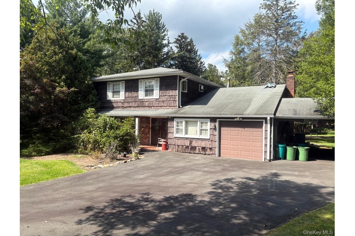 View of front of house with asphalt driveway, a chimney, a garage, and view of scattered trees