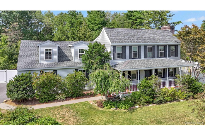 View of front of house with a porch, roof with shingles, a front lawn, and a chimney