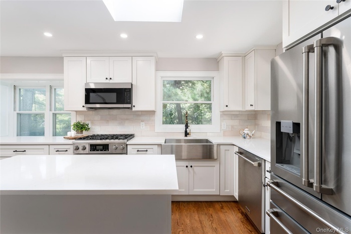 Kitchen with stainless steel appliances, white cabinets, light wood-style flooring, and recessed lighting