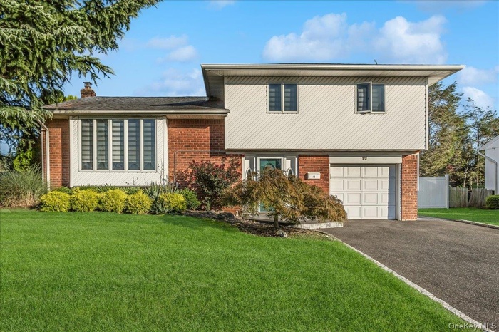 Split level home with brick siding, an attached garage, asphalt driveway, and a chimney