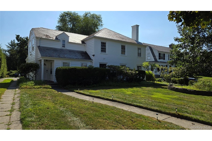 View of front of house featuring a high end roof, a front yard, and a chimney