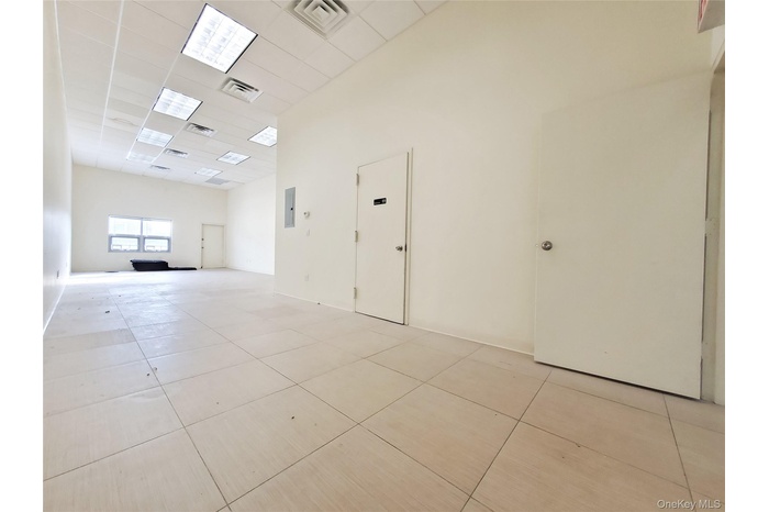 Empty room featuring a paneled ceiling, light tile patterned floors, and electric panel