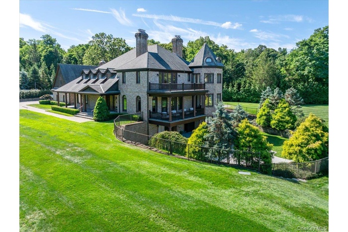 Back of house featuring a balcony, a chimney, brick siding, and view of scattered trees