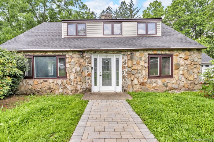 View of front of house featuring stone siding, a shingled roof, a chimney, and a front yard