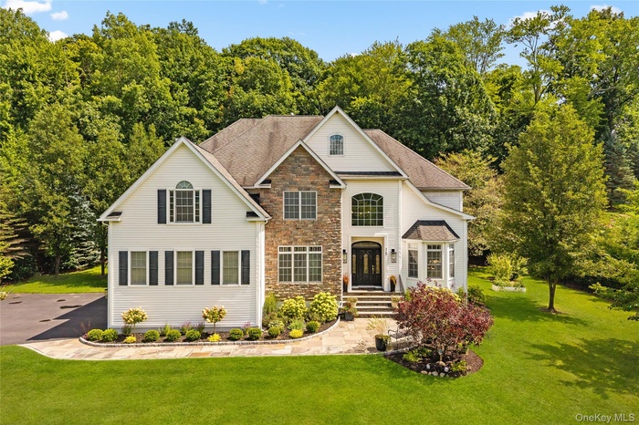 View of front of property with stone siding, a front yard, and a shingled roof