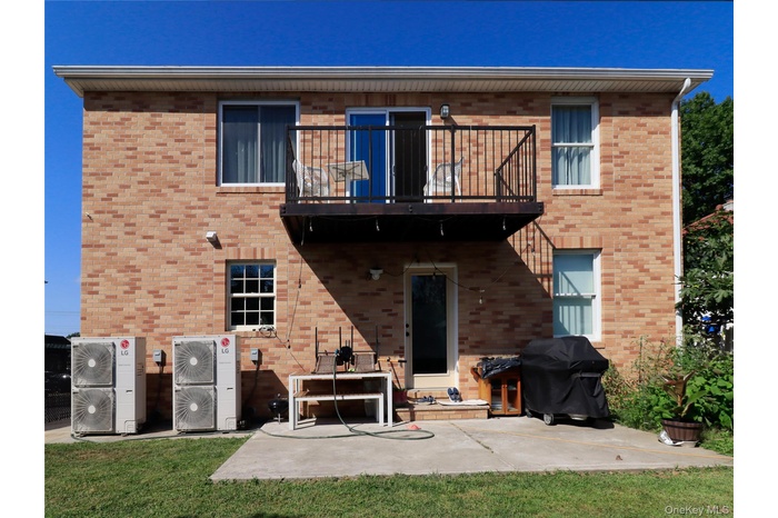 Rear view of property with a patio area, a balcony, a yard, and brick siding