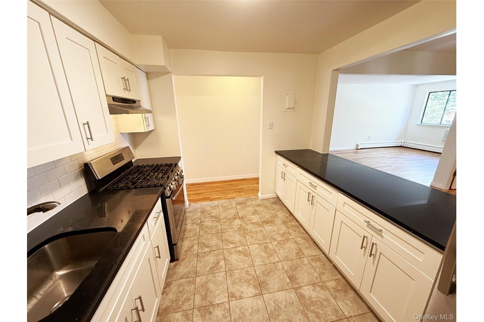 Kitchen featuring stainless steel gas range oven, dark stone countertops, white cabinets, decorative backsplash, and a baseboard heating unit