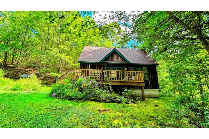 Front view of house featuring a porch, roof with shingles, a wooded view, and a yard
