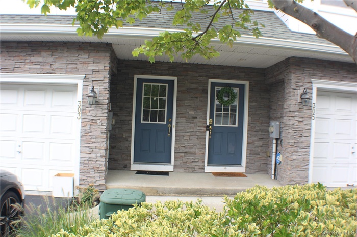 Doorway to property with stone siding, an attached garage, covered porch, and a shingled roof