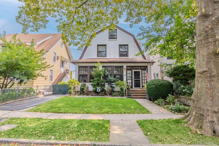 View of front of property with a front lawn, stucco siding, a sunroom, and a gambrel roof