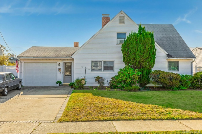 View of front of property featuring a chimney, a front lawn, driveway, an attached garage, and a shingled roof