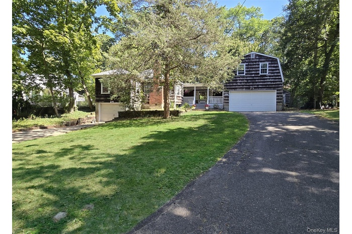 View of front of home featuring a gambrel roof, driveway, an attached garage, a front yard, and covered porch