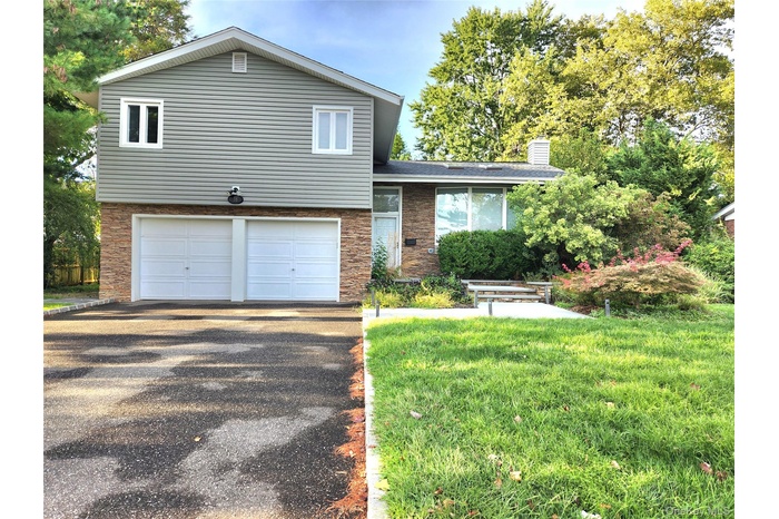 Split level home featuring a front lawn, asphalt driveway, a garage, a chimney, and brick siding
