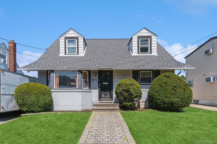 New england style home featuring brick siding, a shingled roof, a front lawn, and a porch