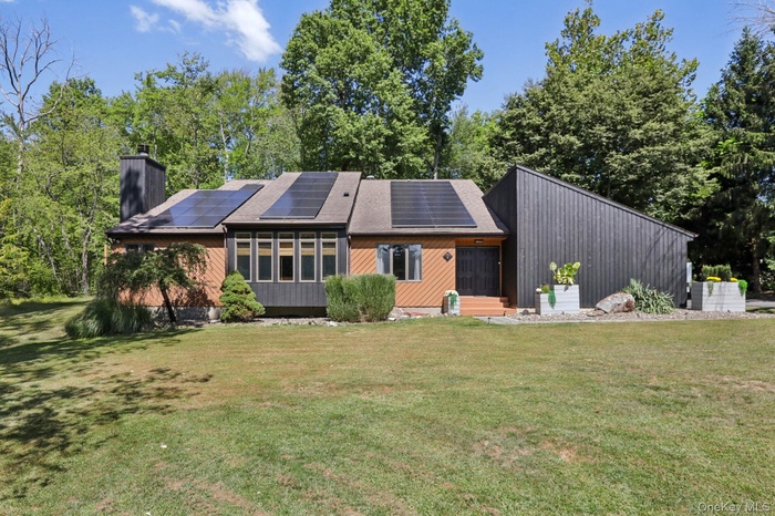 Mid-century inspired home featuring roof mounted solar panels, a chimney, and a front lawn