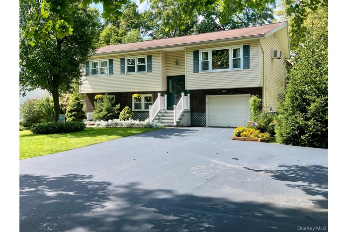 Split foyer home featuring brick siding, driveway, an attached garage, and a front lawn