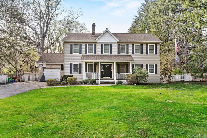 View of front of property with a porch, a chimney, driveway, a garage, and roof with shingles