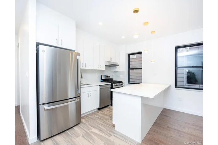 Kitchen featuring stainless steel appliances, decorative light fixtures, light wood-style flooring, white cabinets, and a peninsula