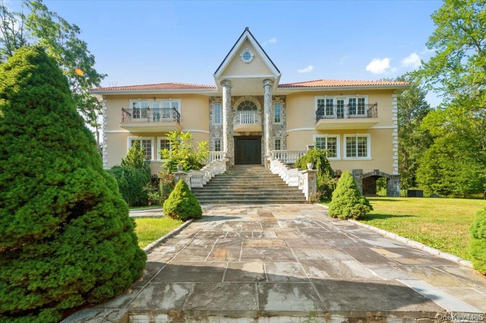View of front of house featuring stucco siding, stone siding, and a balcony