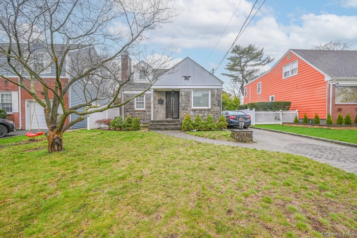 View of front of house with driveway, stone siding, and a chimney