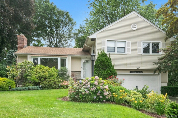 Tri-level home featuring an attached garage, a front lawn, and a chimney