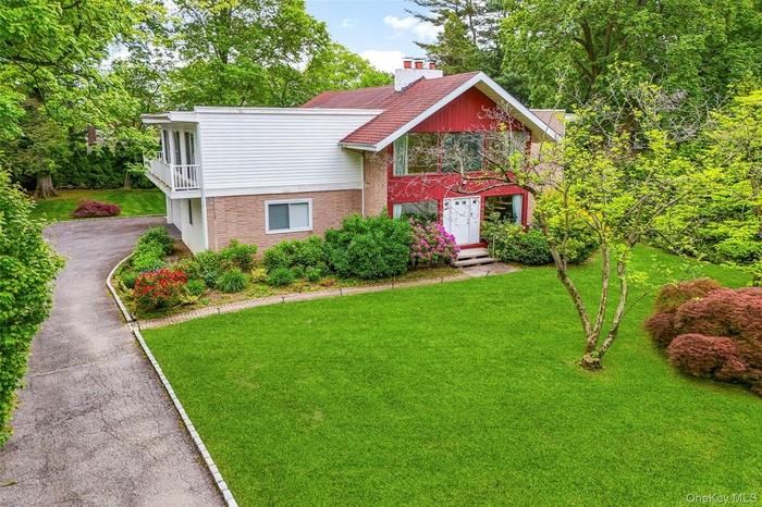 View of front of property featuring a front yard, brick siding, asphalt driveway, and a chimney