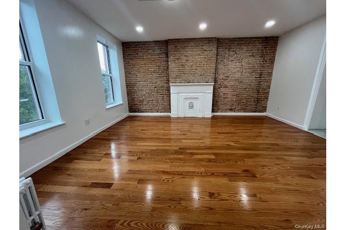 Unfurnished living room featuring brick wall, light wood-style floors, and recessed lighting