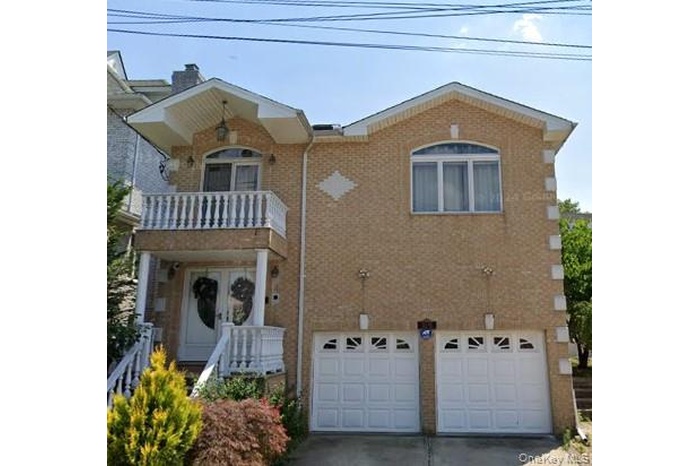 View of front of home featuring a balcony, brick siding, a garage, concrete driveway, and a chimney