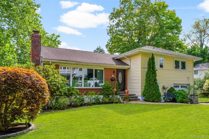Split level home with a garage, a front lawn, a chimney, brick siding, and a shingled roof