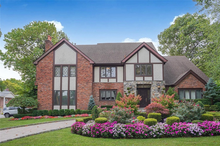 Tudor-style house featuring stone siding, a chimney, brick siding, stucco siding, and a shingled roof