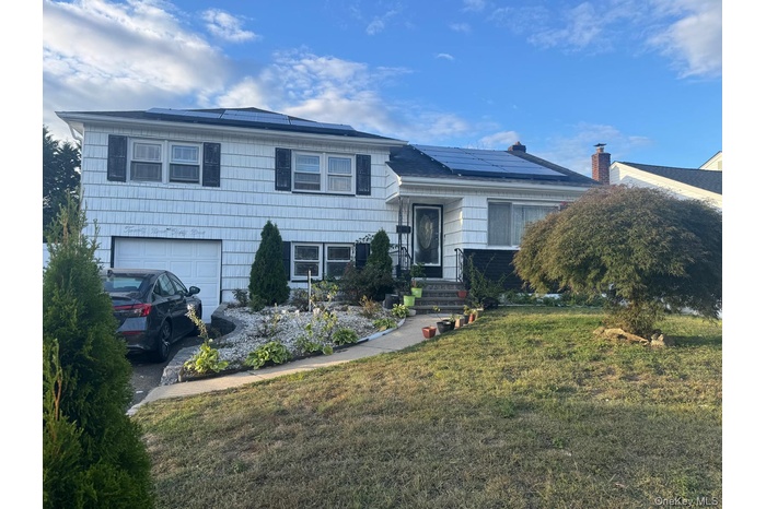 Split level home featuring solar panels, a front lawn, and a garage