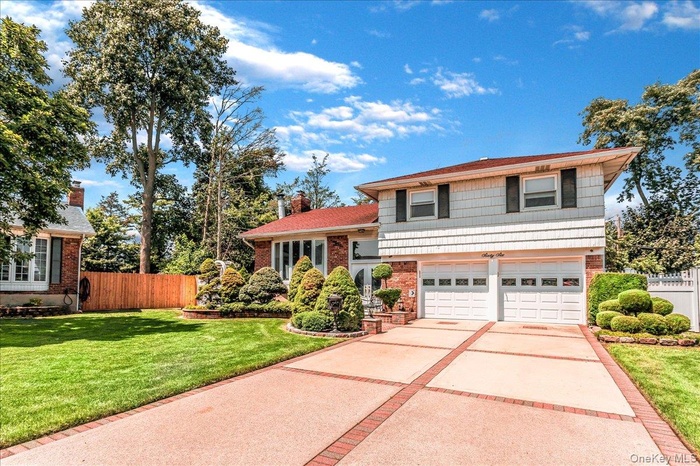 Tri-level home featuring driveway, brick siding, a garage, and a chimney