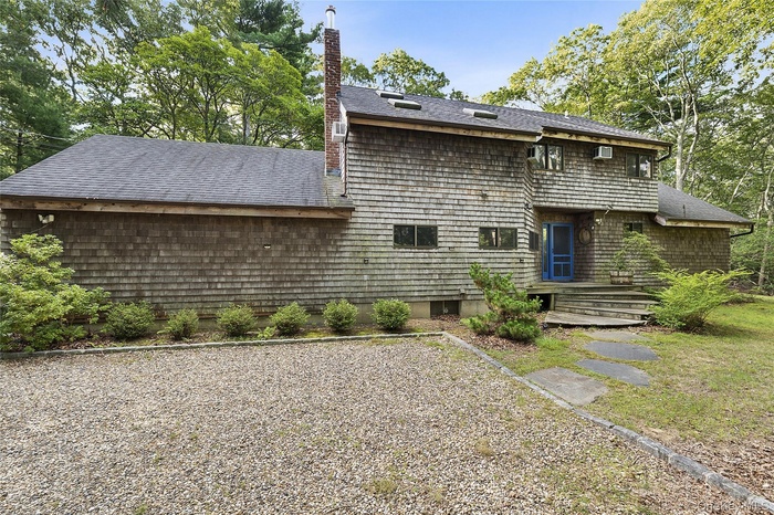 Back of property with a chimney and a shingled roof